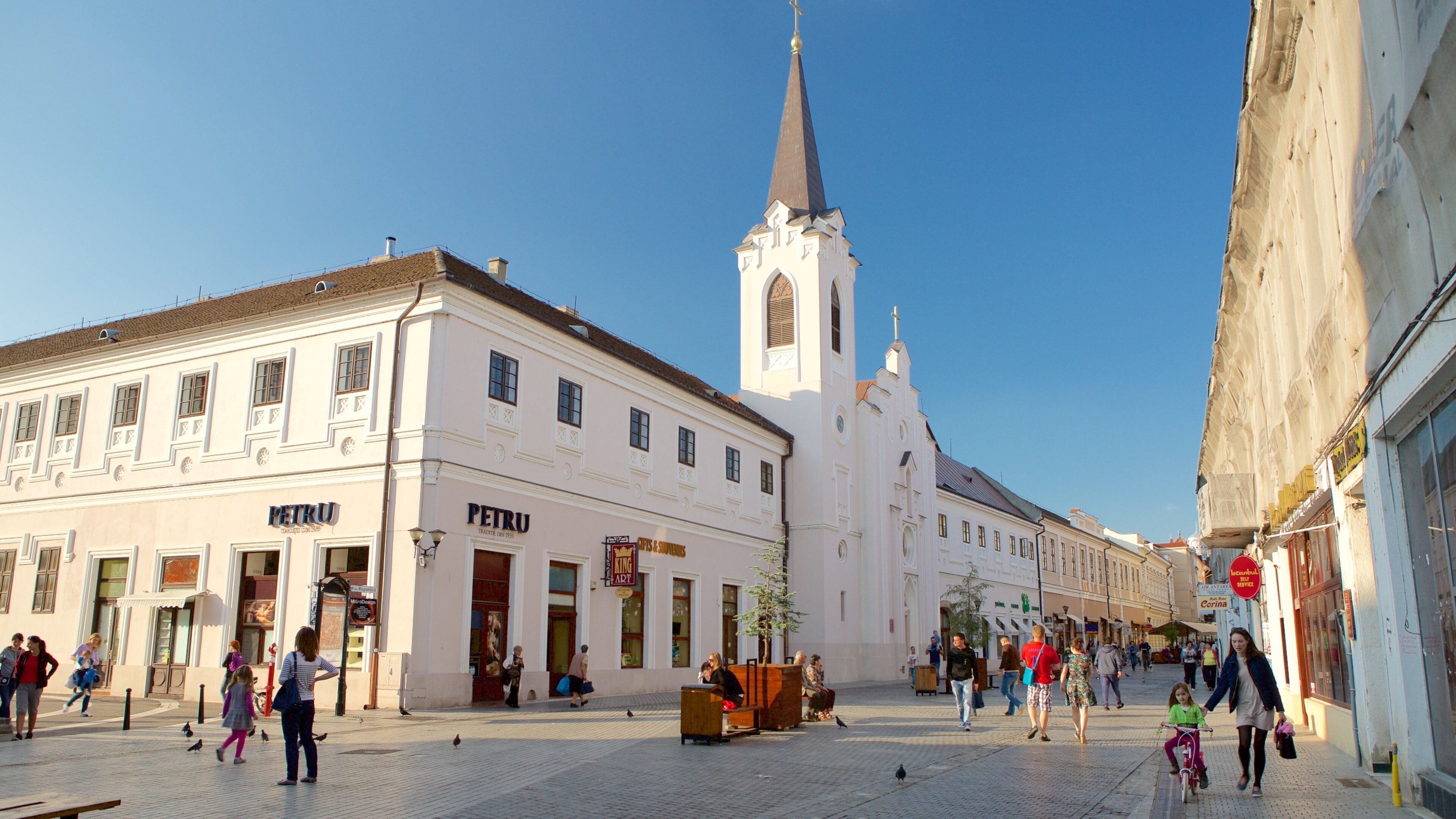 A cobblestone square with historic buildings, a church tower, and pedestrians.