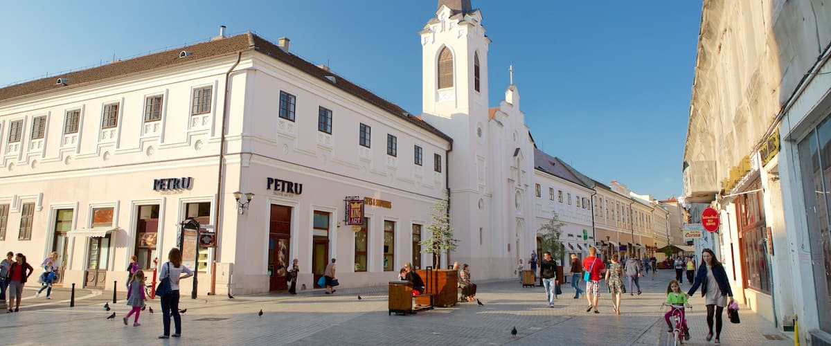 A cobblestone square with historic buildings, a church tower, and pedestrians.