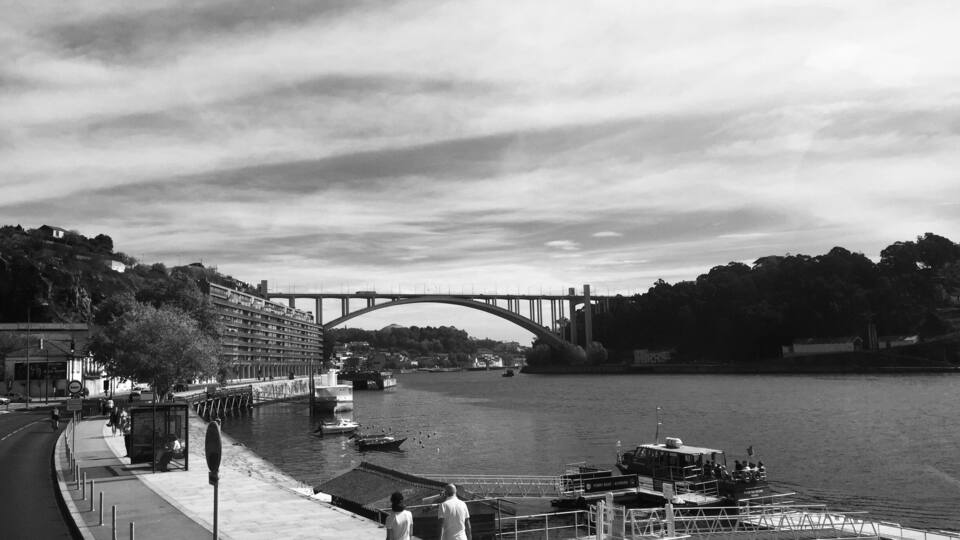 A river with a bridge, boats, and a pedestrian walkway.