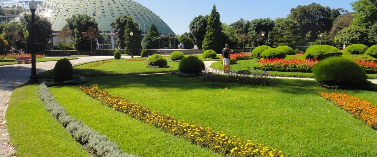 A large green dome structure surrounded by manicured gardens with neatly trimmed hedges and flower beds.