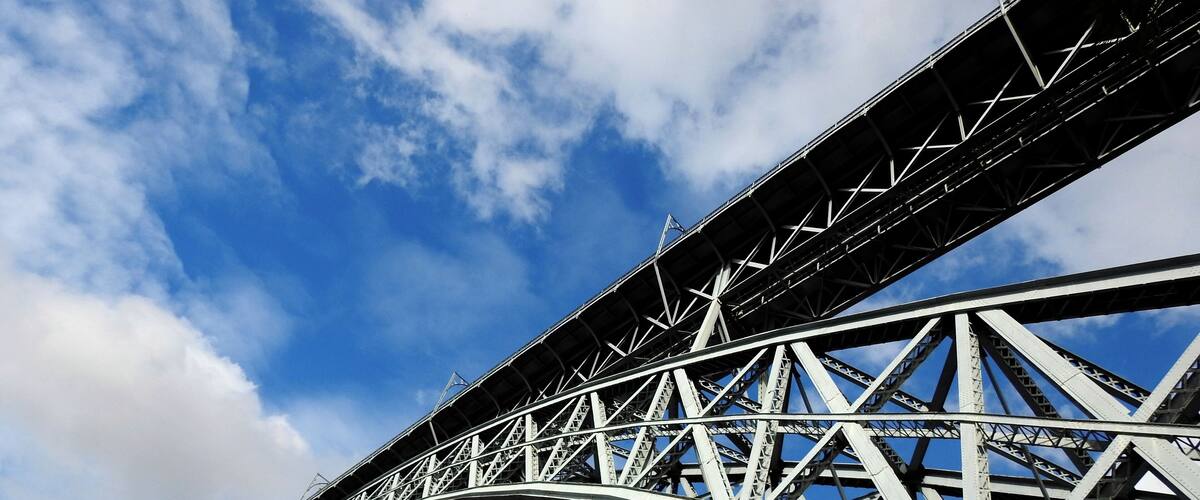 A steel bridge with a curved arch against a blue sky with clouds.