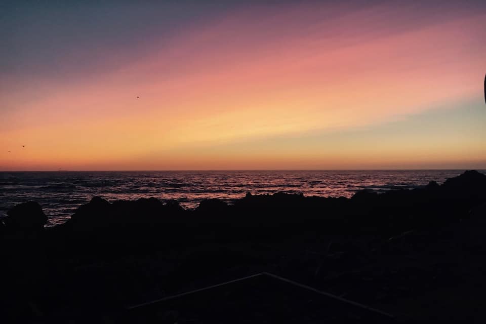 A sunset over the ocean with silhouettes of rocks in the foreground.