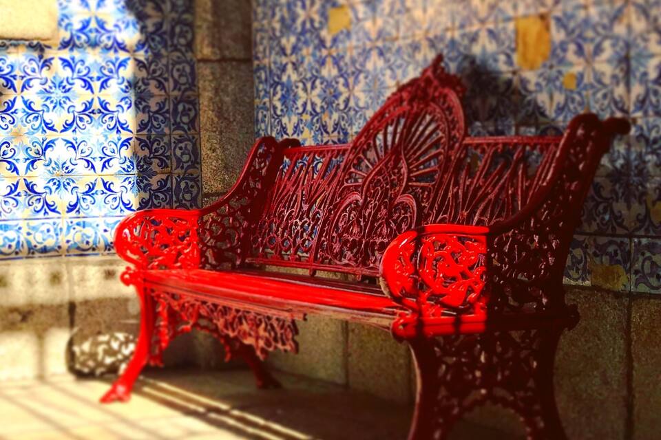 A red bench with intricate carvings against a blue and white tiled wall.