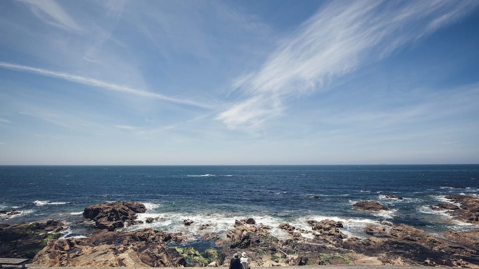 A rocky coastline with waves crashing against the rocks under a clear sky.