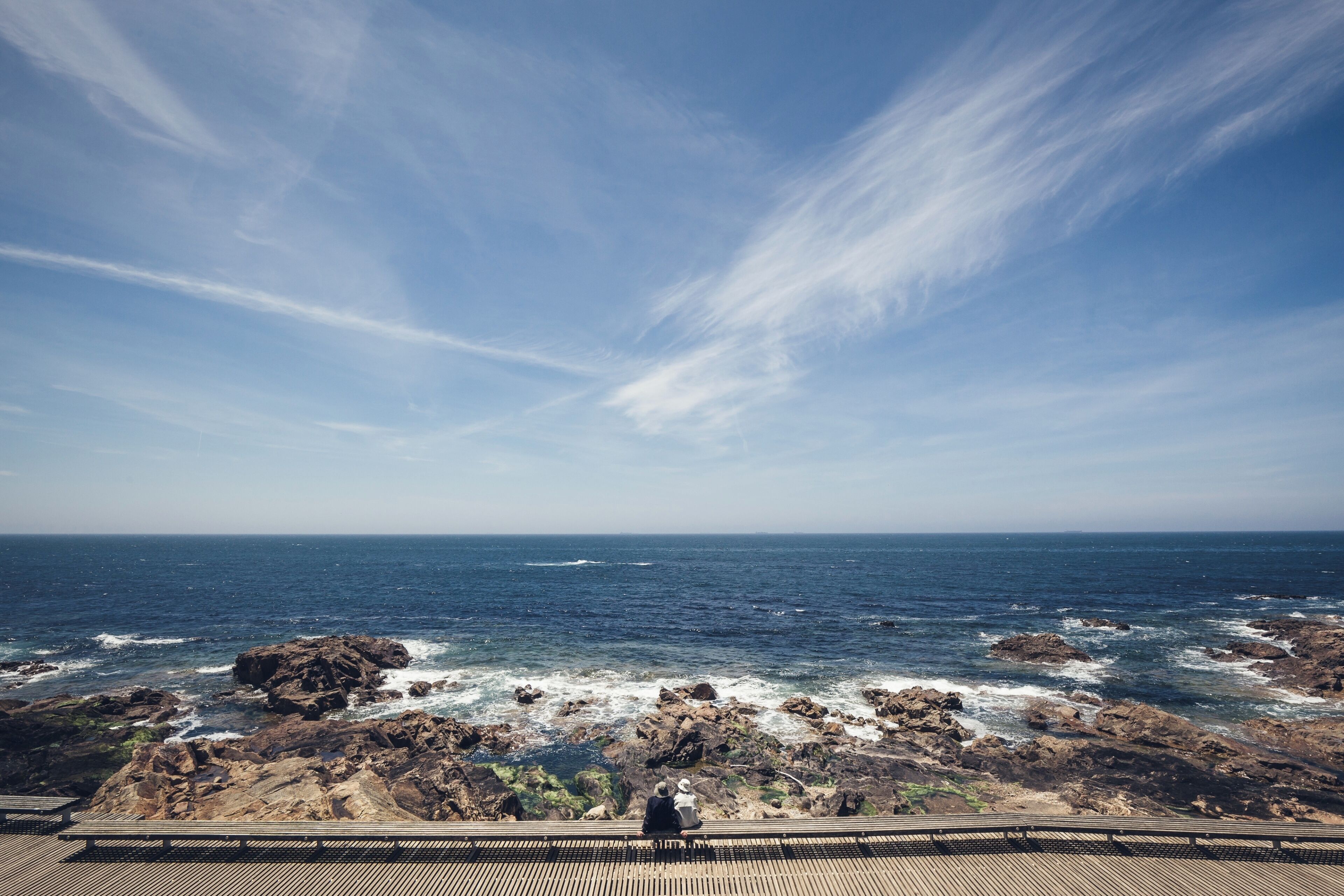 A rocky coastline with waves crashing against the rocks under a clear sky.