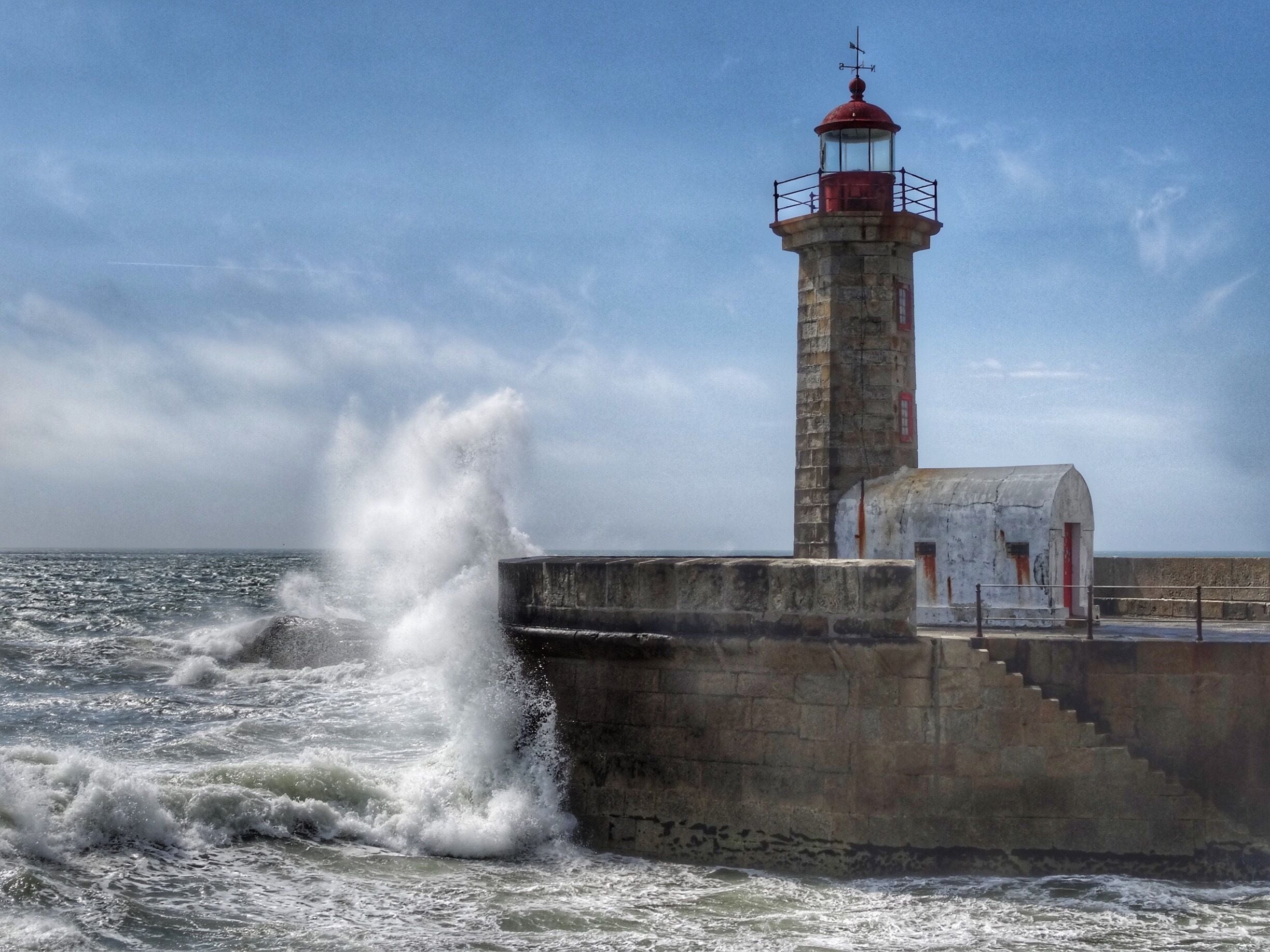 A lighthouse by the sea with waves crashing against the shore.