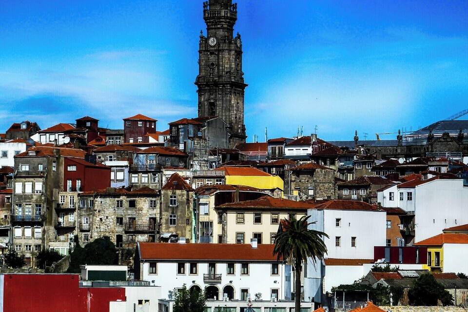 Uma cidade histórica com uma torre do relógio imponente, edifícios coloridos e um céu azul claro.