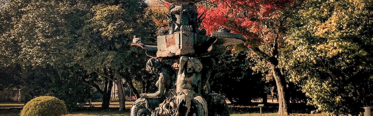 Una fuente escalonada con estatuas en un parque con follaje otoñal.