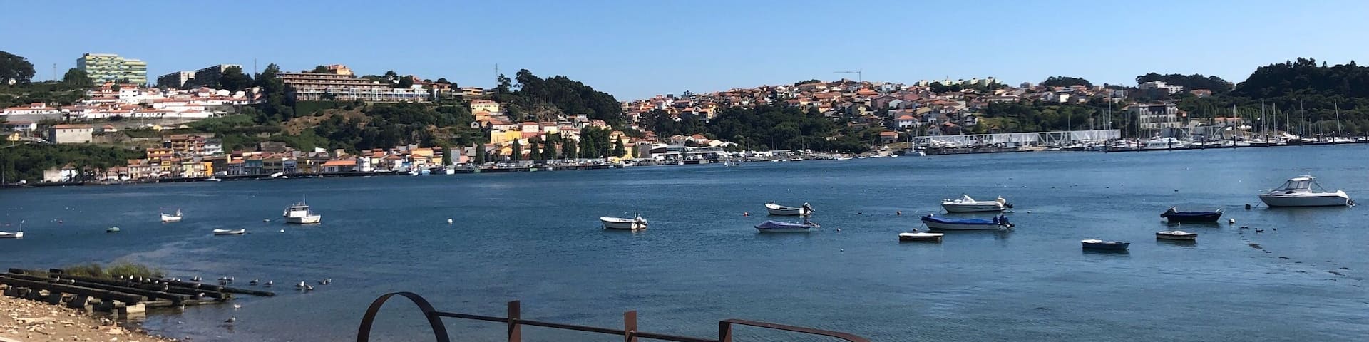 A coastal town with boats on the water and a metal railing in the foreground.