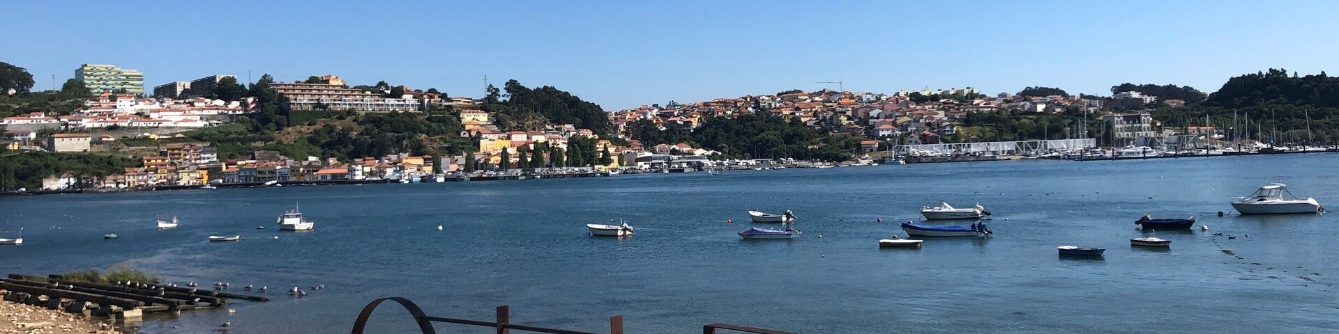 Un pueblo costero con barcos en el agua y una baranda metálica al frente.