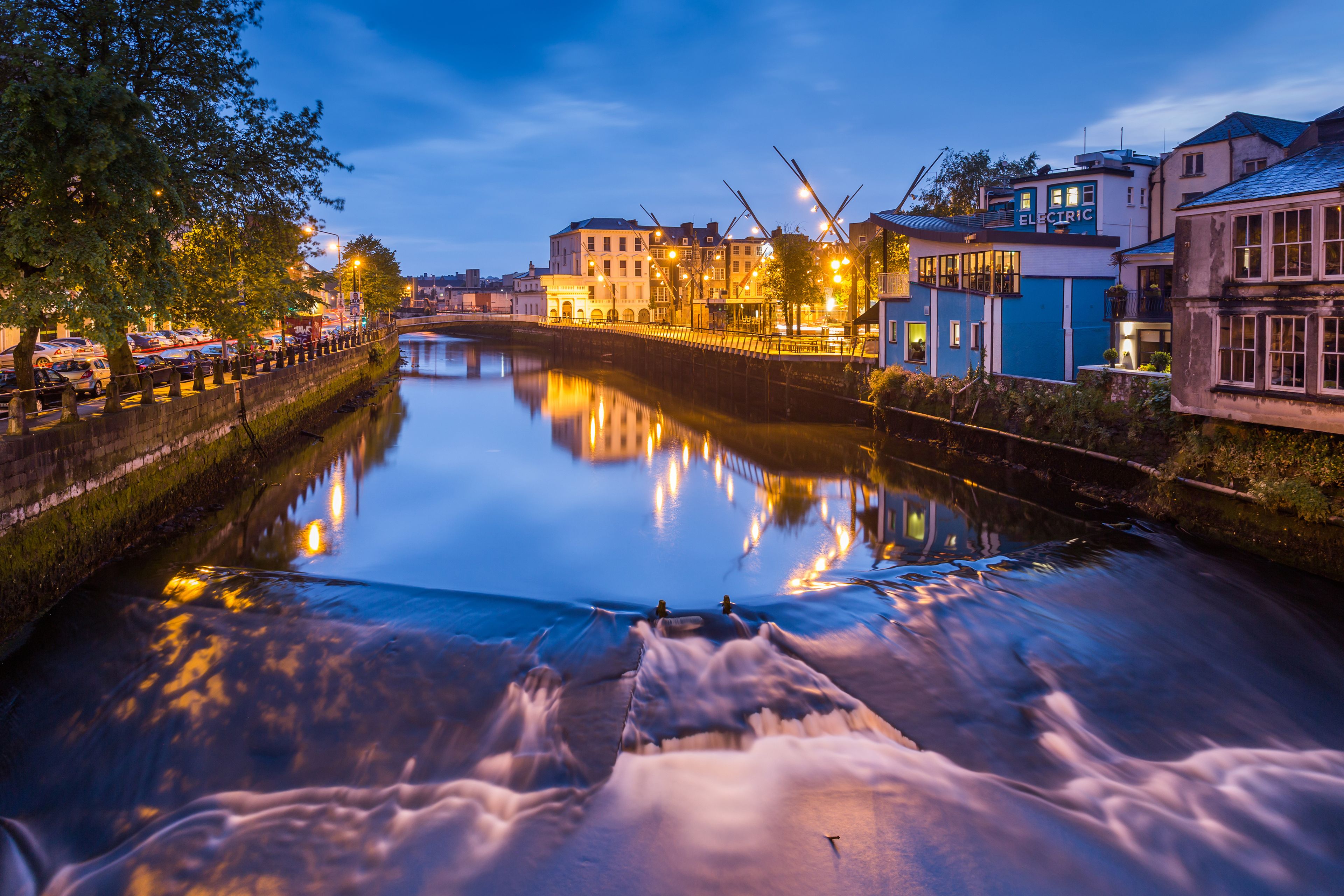A river reflecting city lights, a bridge, and buildings along the riverbank.