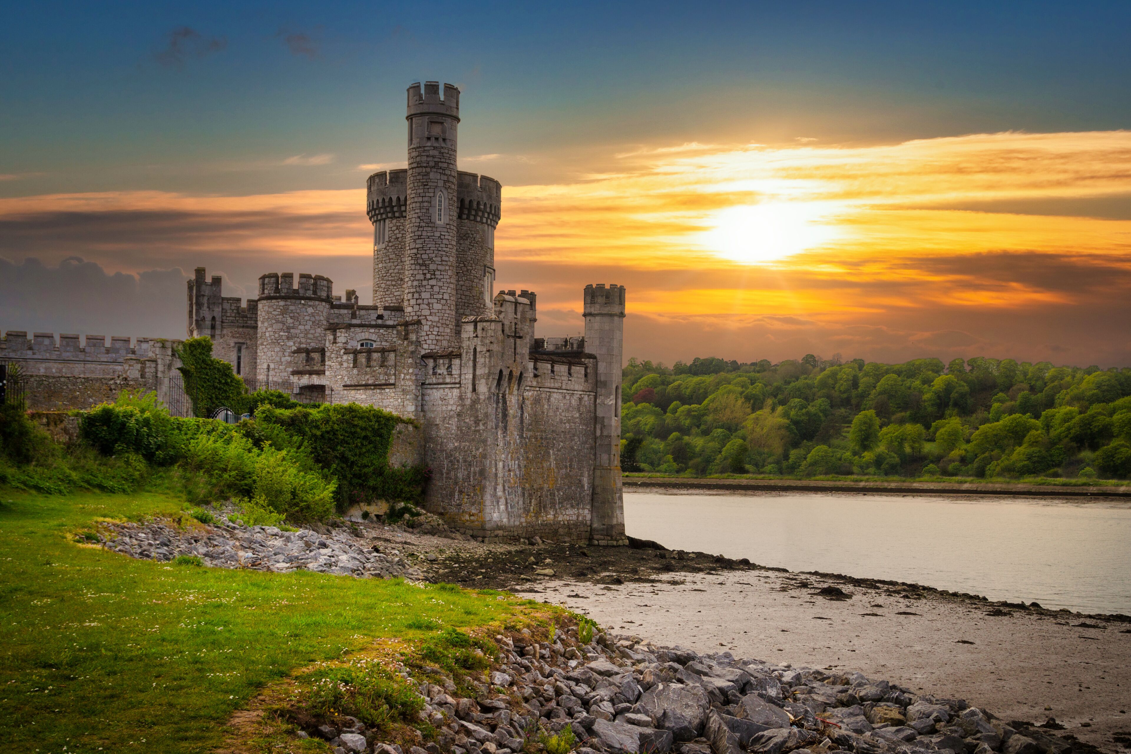 A historic castle by a river at sunset.