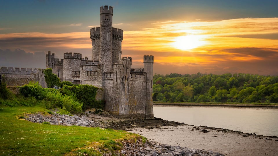 A historic castle by a river at sunset.