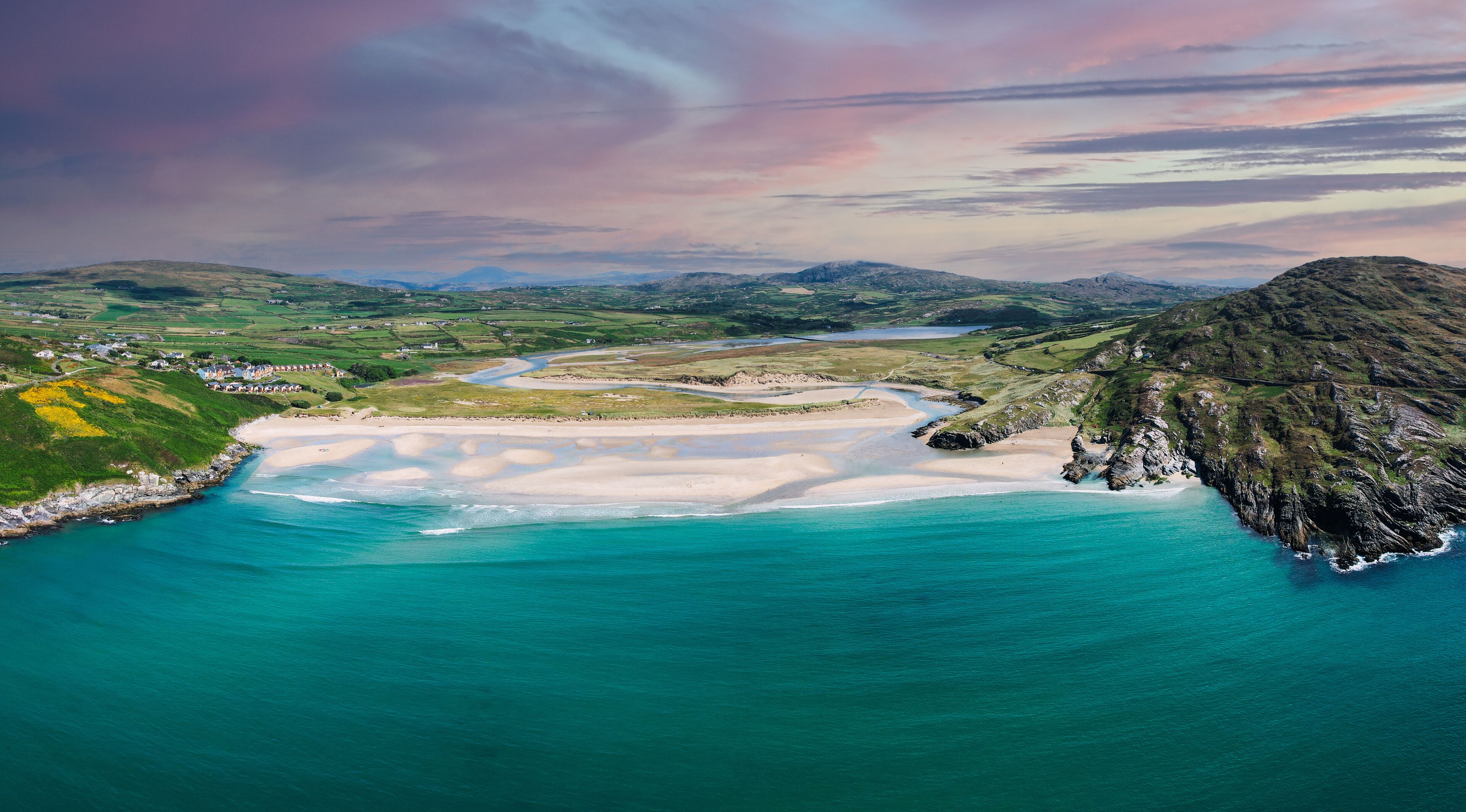 A coastal landscape with a sandy beach, turquoise waters, and rolling hills.