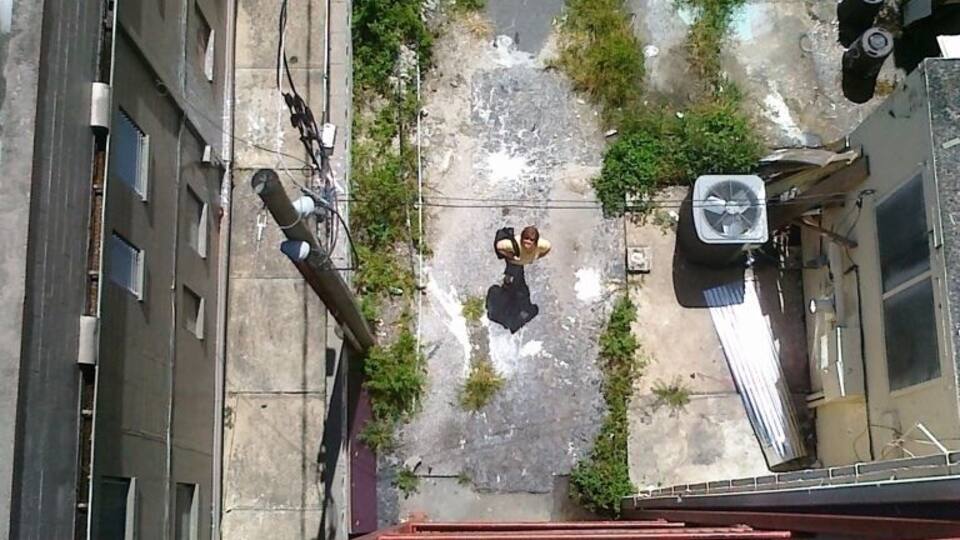 Vista aérea de uma rua urbana com edifícios, um rio e uma ponte para pedestres.