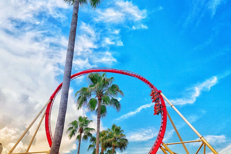 Une montagne russe située au parc Universal Orlando Resort, avec un grand palmier et un ciel d’un bleu éclatant.
