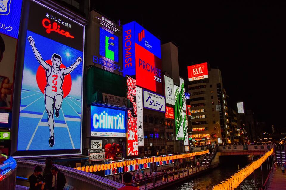 A brightly lit urban area with illuminated billboards and a river.