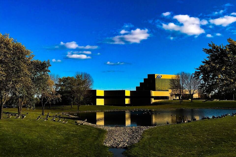 Ein Park mit Teich, Bäumen und einem modernen Gebäude in Gelb und Schwarz.