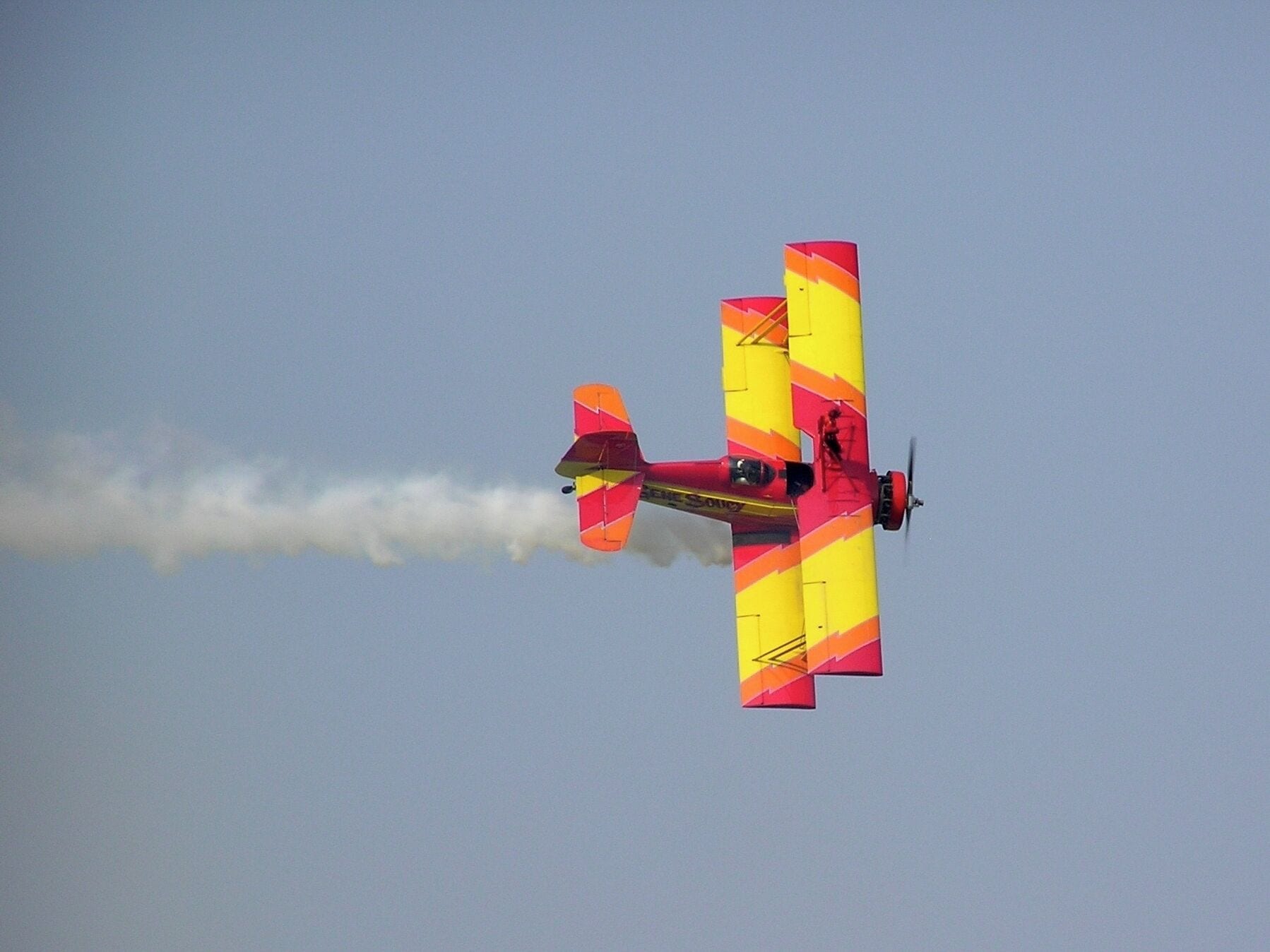 A colorful biplane with red and yellow stripes flying in a clear sky.