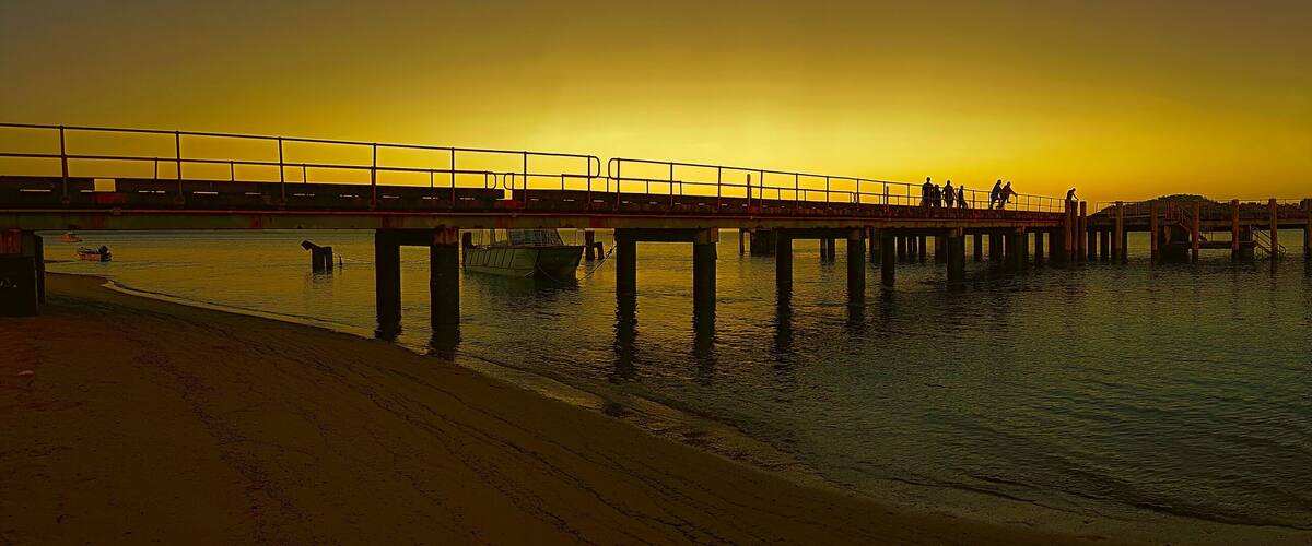 A sunset over a pier with people walking and a boat in the water.
