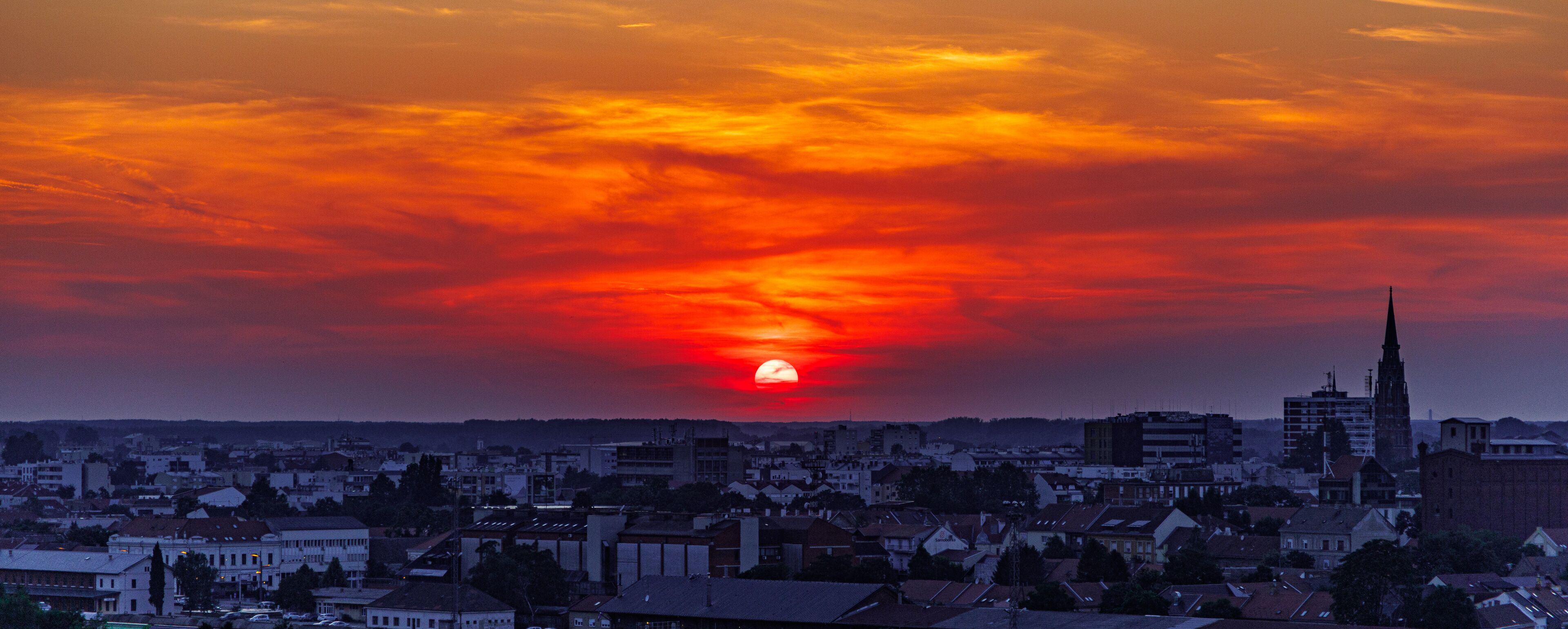 A sunset over a cityscape with a prominent church spire.