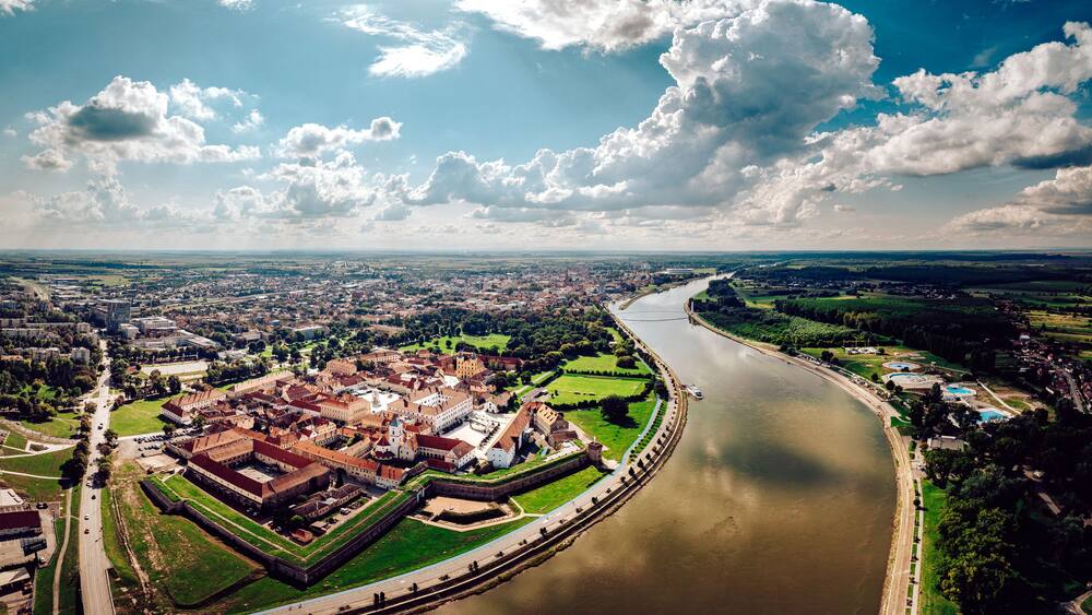 Vue aérienne d’une ville historique, avec une rivière, un château fort et la verdure environnante.