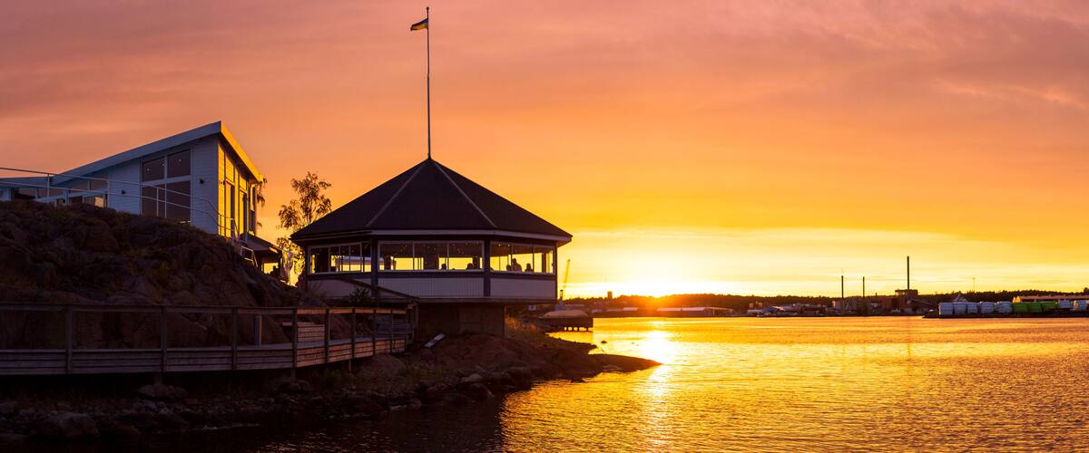 A sunset over a body of water with a gazebo and a building on the shore.