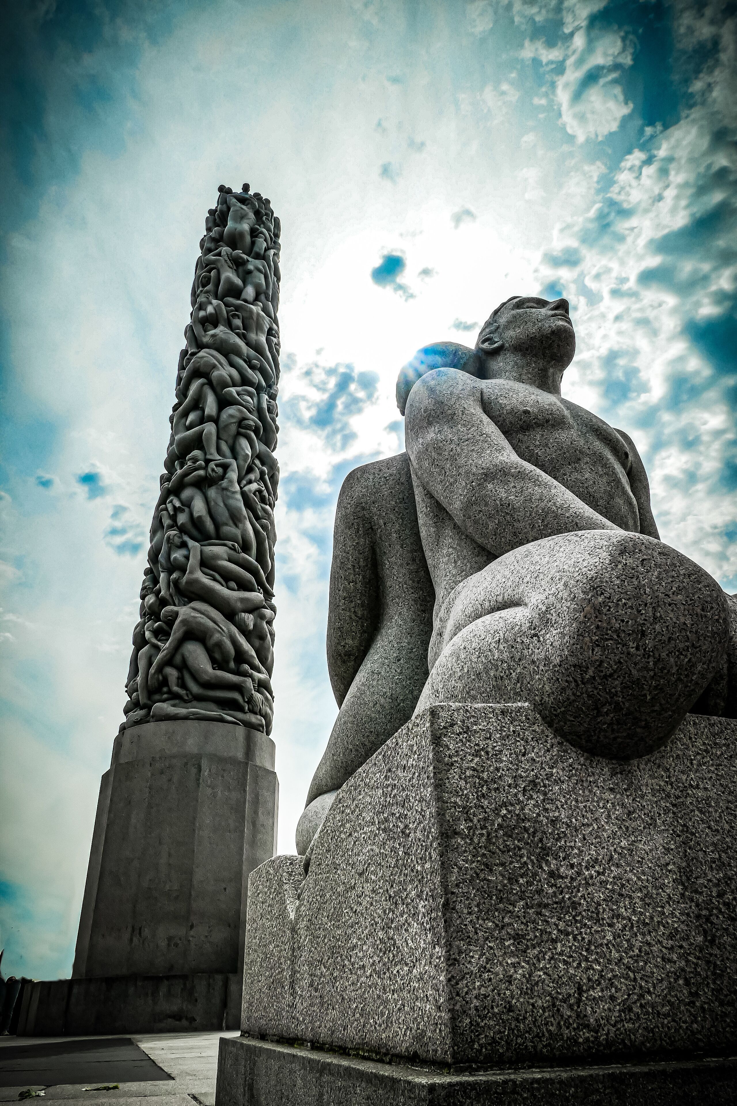 A stone sculpture of a reclining figure and a tall pillar with intricate carvings.