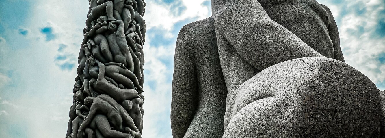 Una escultura de piedra que representa una figura reclinada y un alto pilar con intrincados grabados.