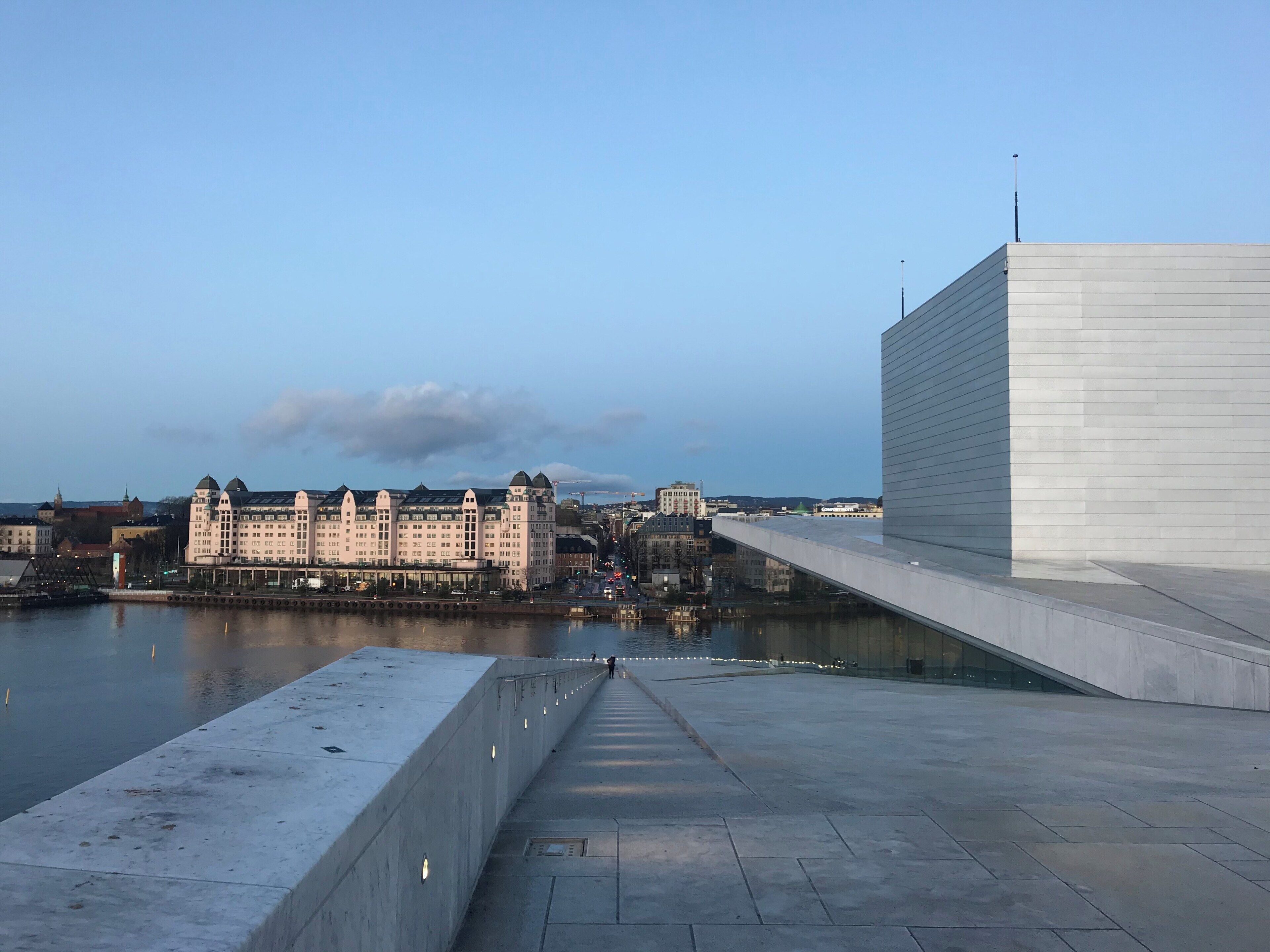 Un paseo marítimo con un edificio moderno y arquitectura histórica al fondo.