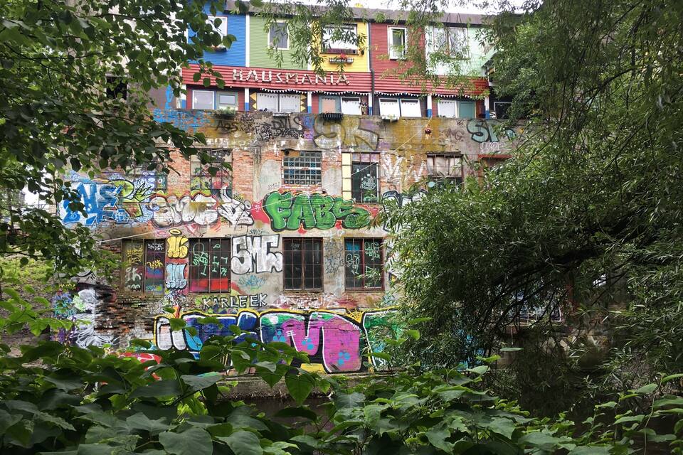 A multi-story building with colorful graffiti and overgrown vegetation.