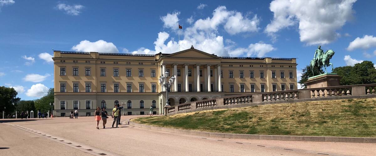 A large neoclassical building with a central pediment and columns, a statue of a figure on horseback, and a clear blue sky with scattered clouds.