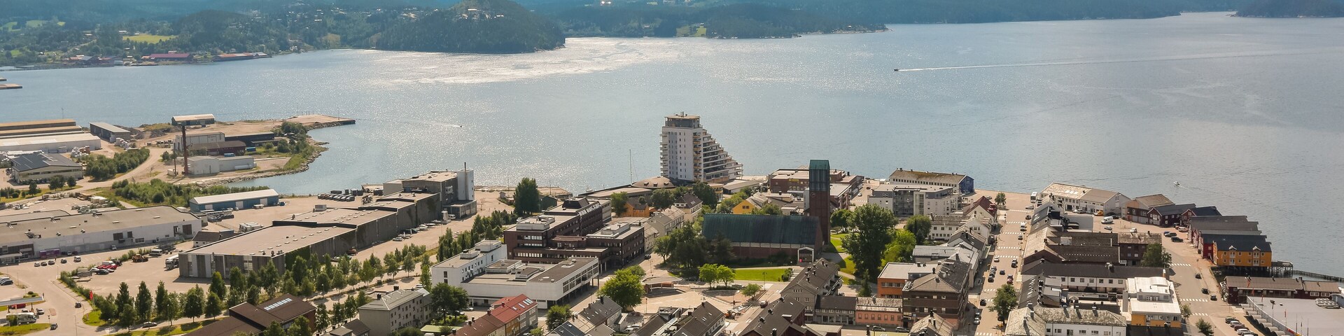 Un pueblo a orillas del lago con una iglesia destacada, un edificio alto y colinas circundantes.
