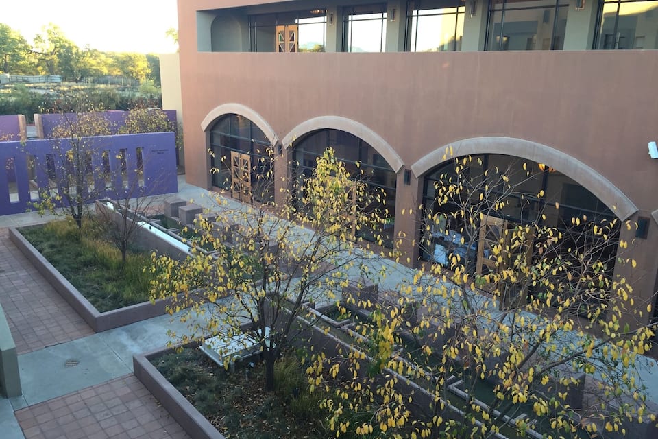A modern building with arched windows and a landscaped courtyard with trees and a pathway.