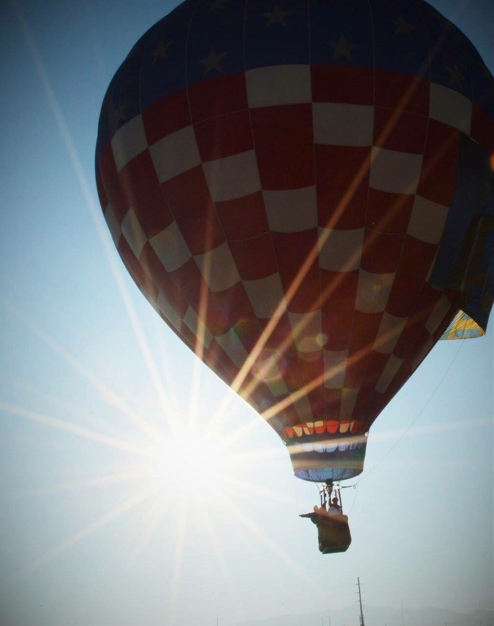 A hot air balloon with a checkered pattern, flying against a clear sky with the sun shining.