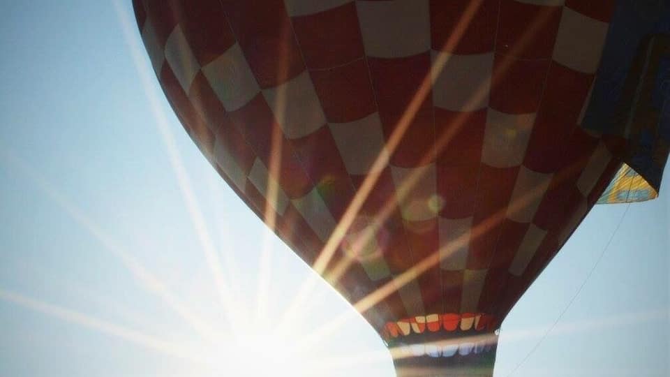 A hot air balloon with a checkered pattern, flying against a clear sky with the sun shining.