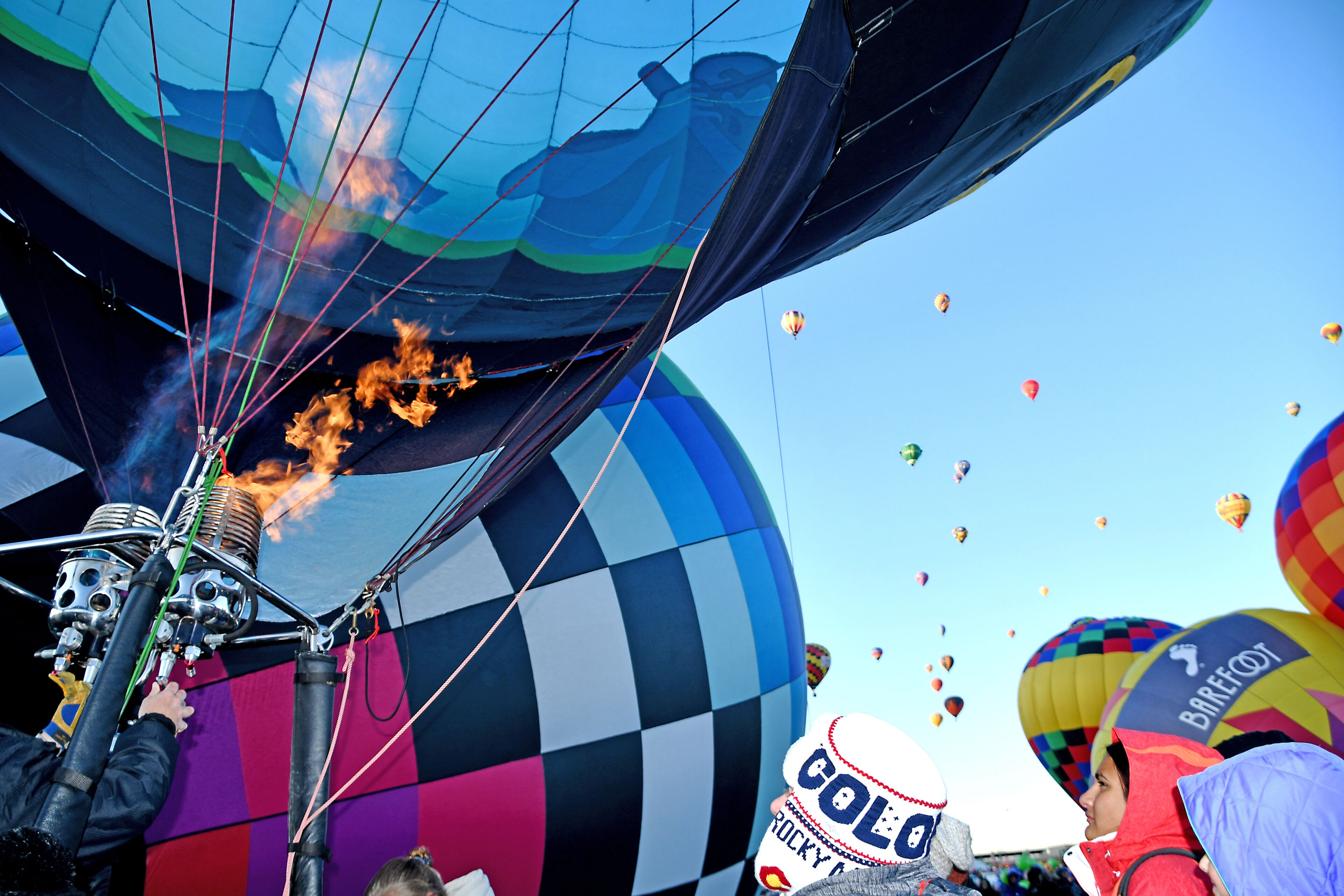 A hot air balloon with flames, surrounded by colorful balloons in a clear sky.
