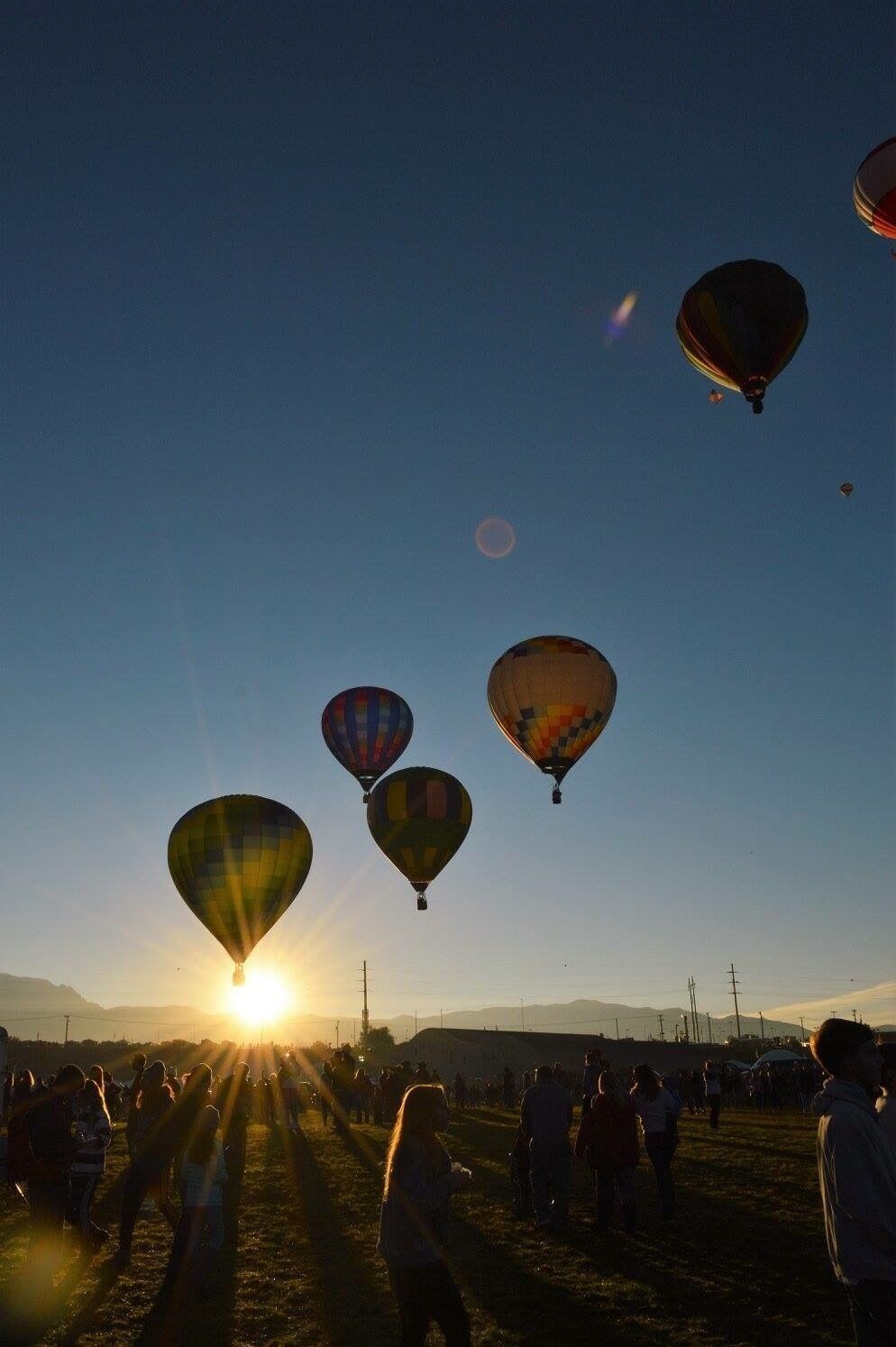 A sunset with hot air balloons in the sky and people on the ground.