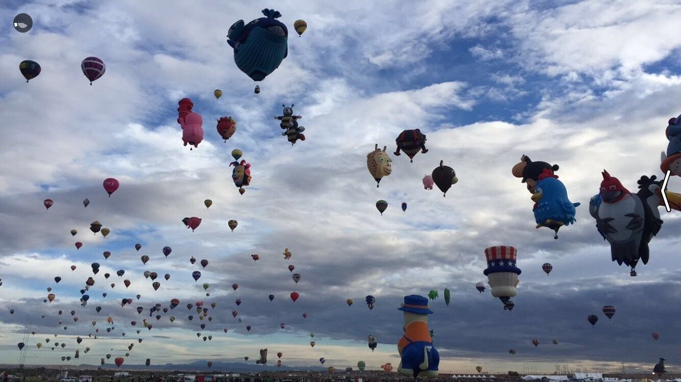En himmel fyldt med luftballoner i forskellige former og farver mod en overskyet himmel.