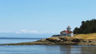 Um farol sobre um afloramento rochoso à beira-mar, com montanhas ao fundo.