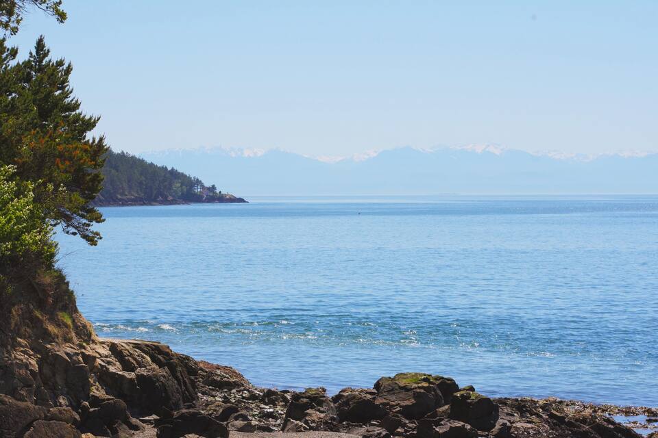 Un rivage rocheux, une mer calme et des montagnes à l’horizon.