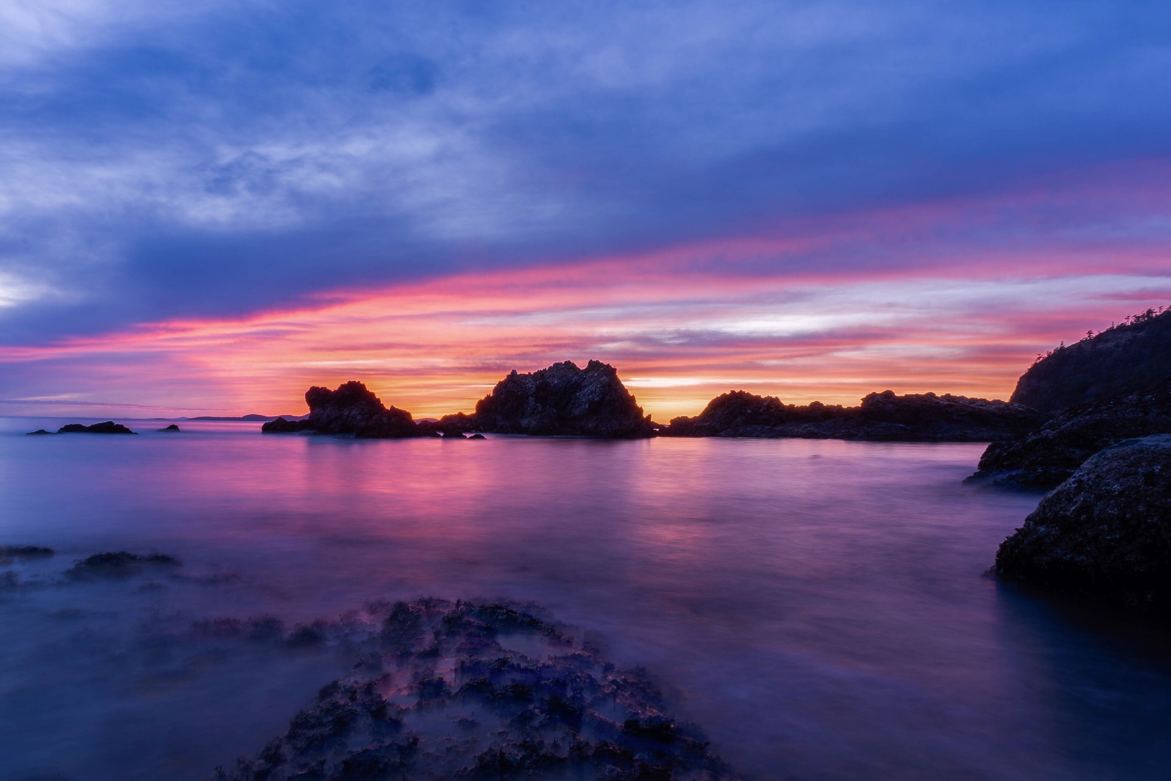 A coastal landscape with rocky formations and a colorful sunset sky.