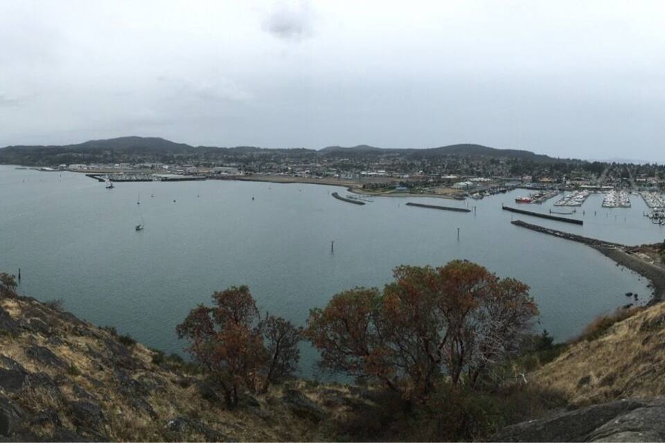 A coastal landscape with a large body of water, rocky terrain, and sparse vegetation.