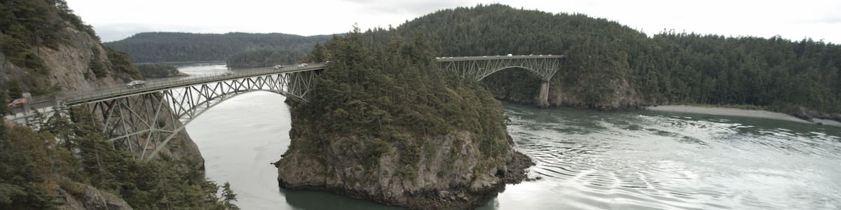 Eine Stahlbrücke überspannt einen Fluss, umgeben von bewaldeten Hügeln.