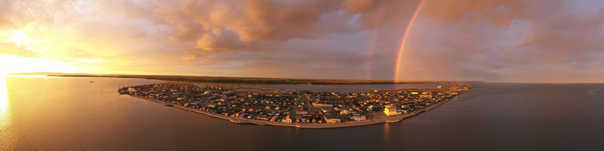 An aerial view of a coastal town with a rainbow over the water.
