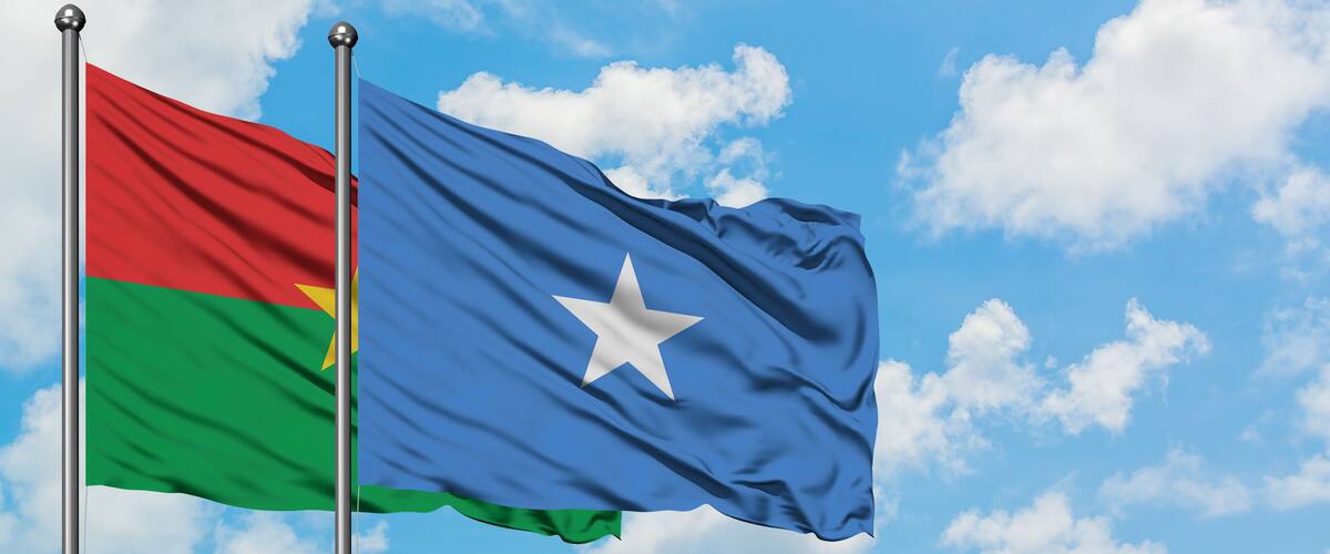 Two flags waving against a blue sky with clouds.