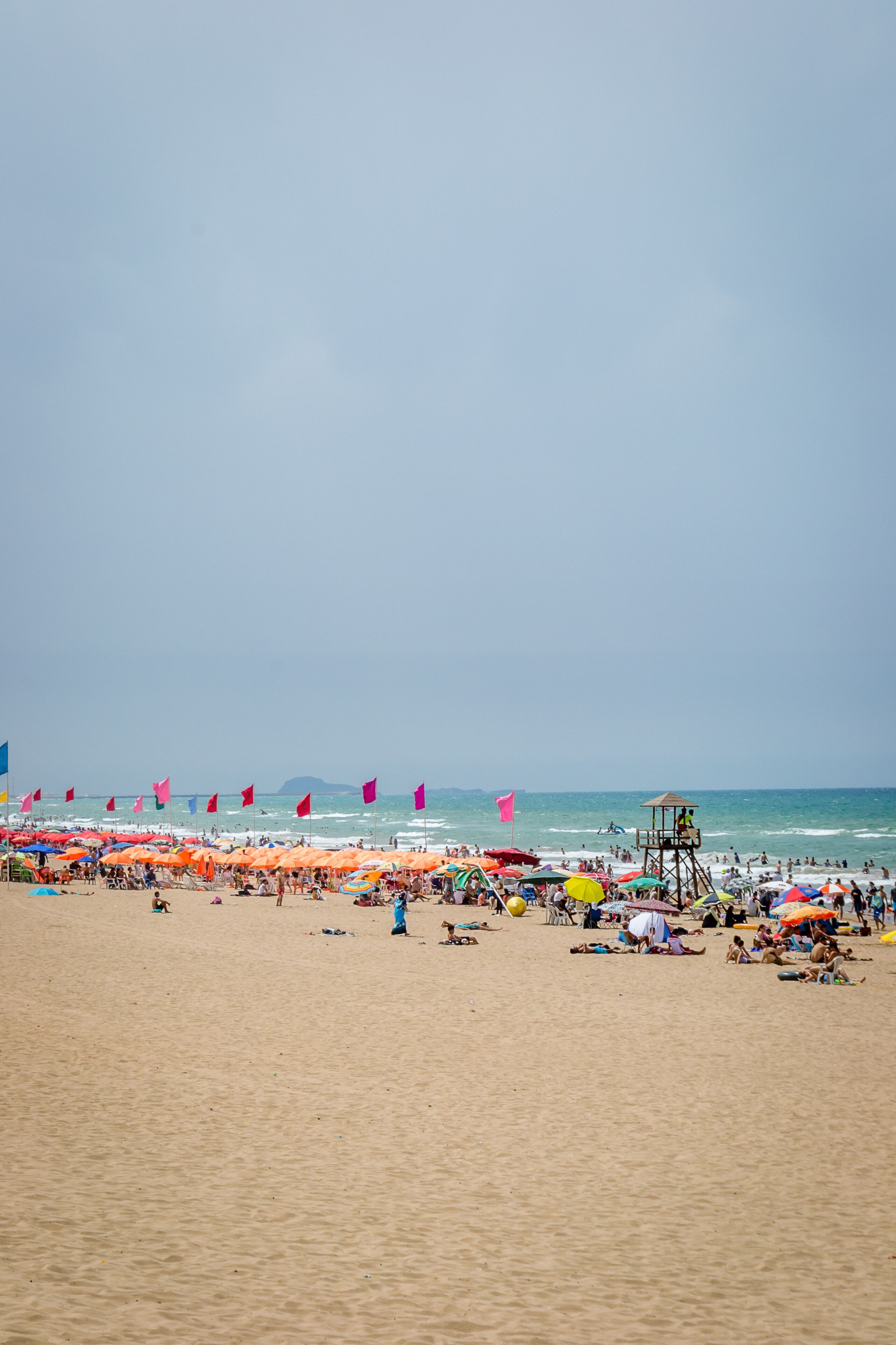A crowded beach with numerous colorful umbrellas and a lifeguard tower.