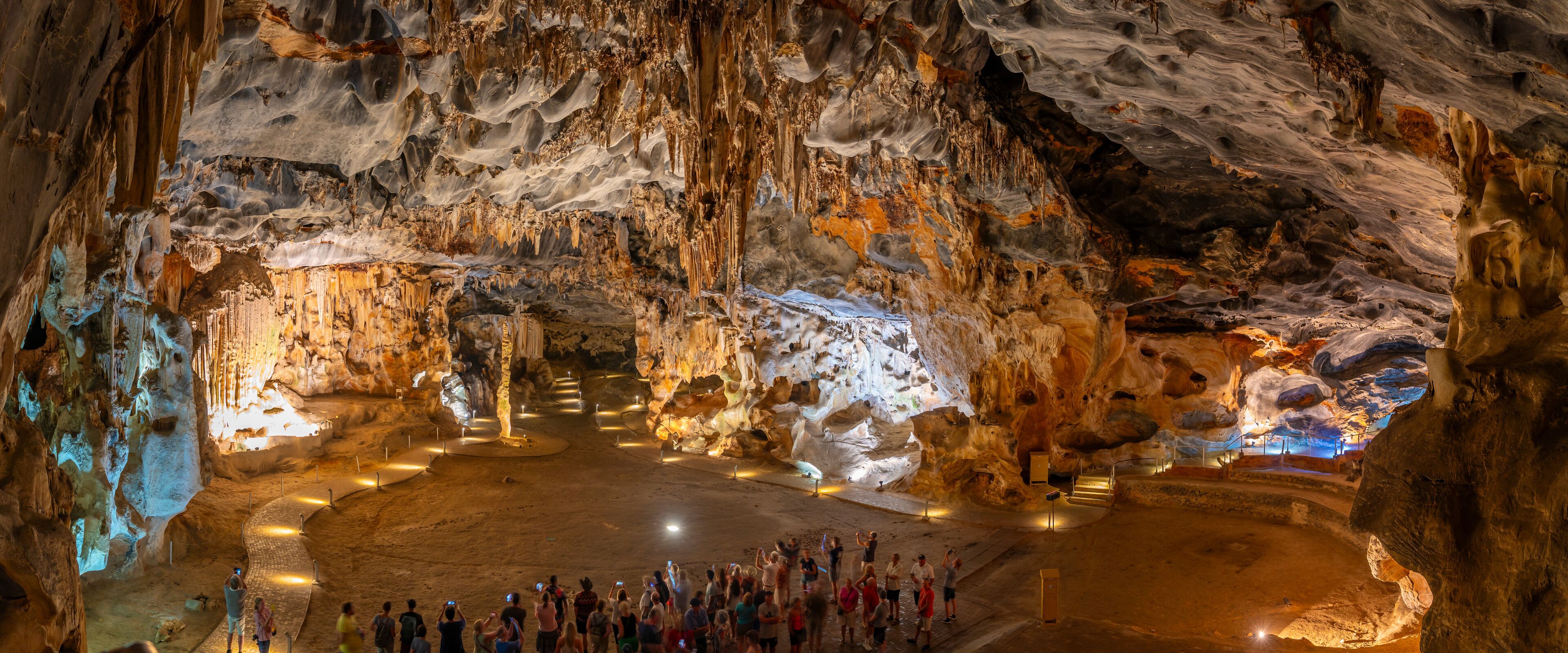 A cave with stalactites and stalagmites, a central open area, and visitors.