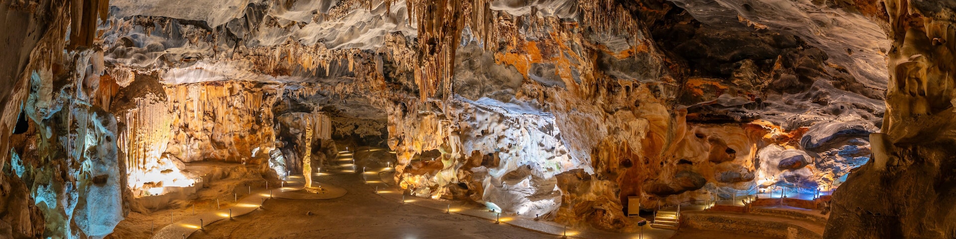 Una cueva con estalactitas y estalagmitas, un espacio central abierto y visitantes.