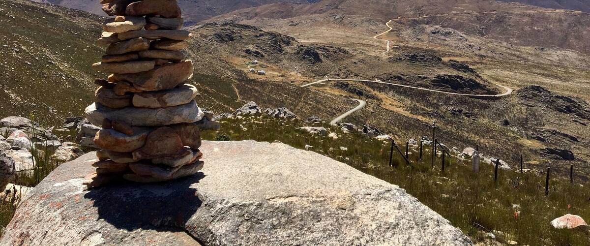 A stone cairn on a mountain ridge overlooking a winding road and distant hills.